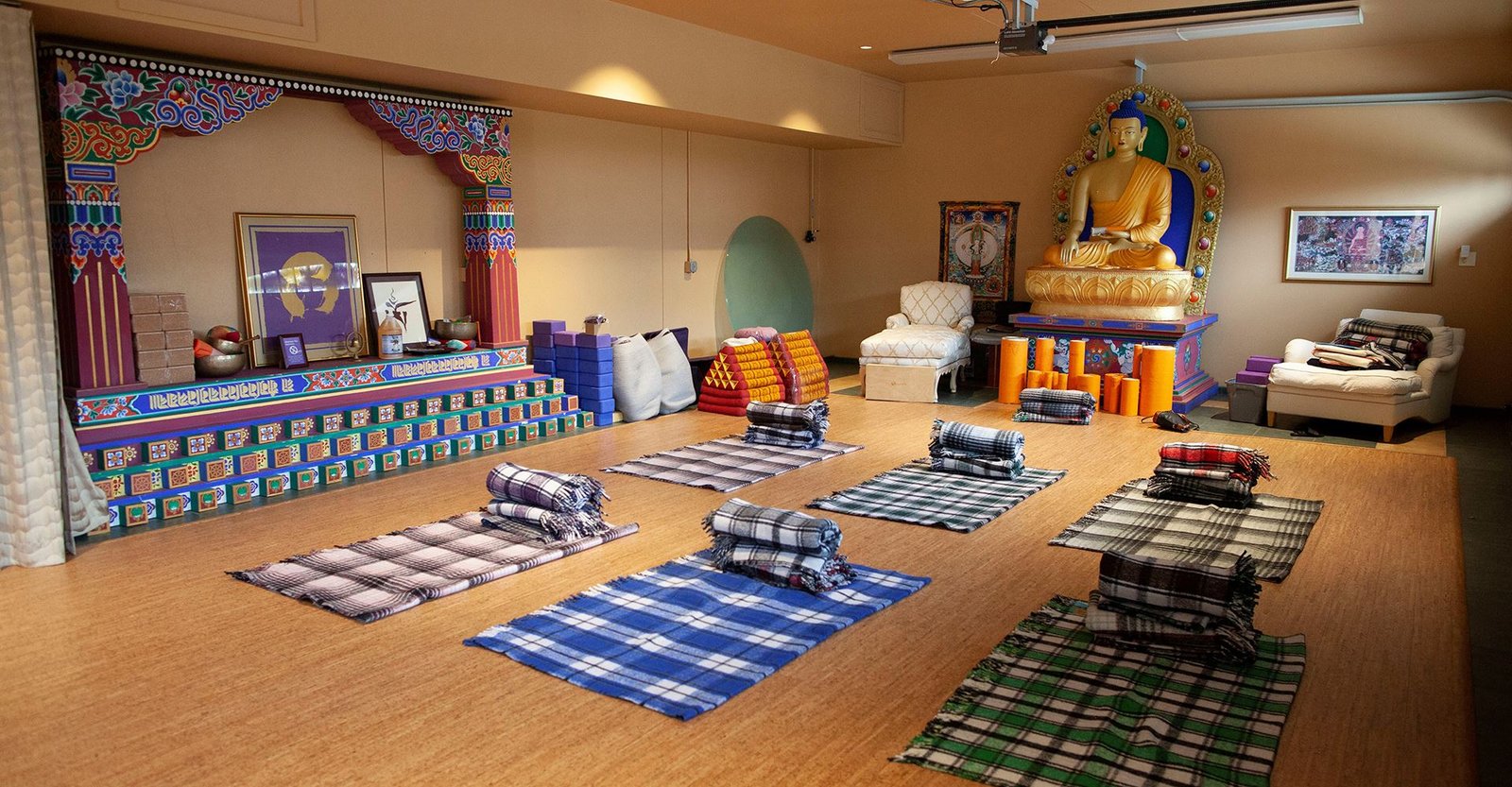 The meditation hall at Harmony Mountain, with a golden Buddha, Tibetan decoration and blankets laid out for practice
