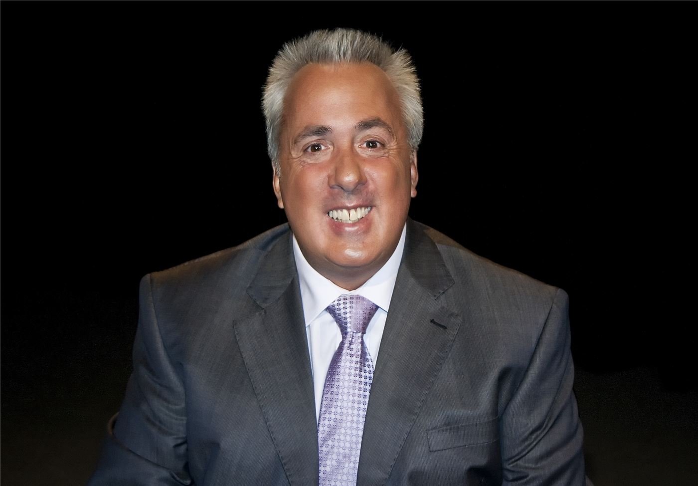 Dr. Peter Amato in a grey suit and lilac tie, smiling, in a television studio